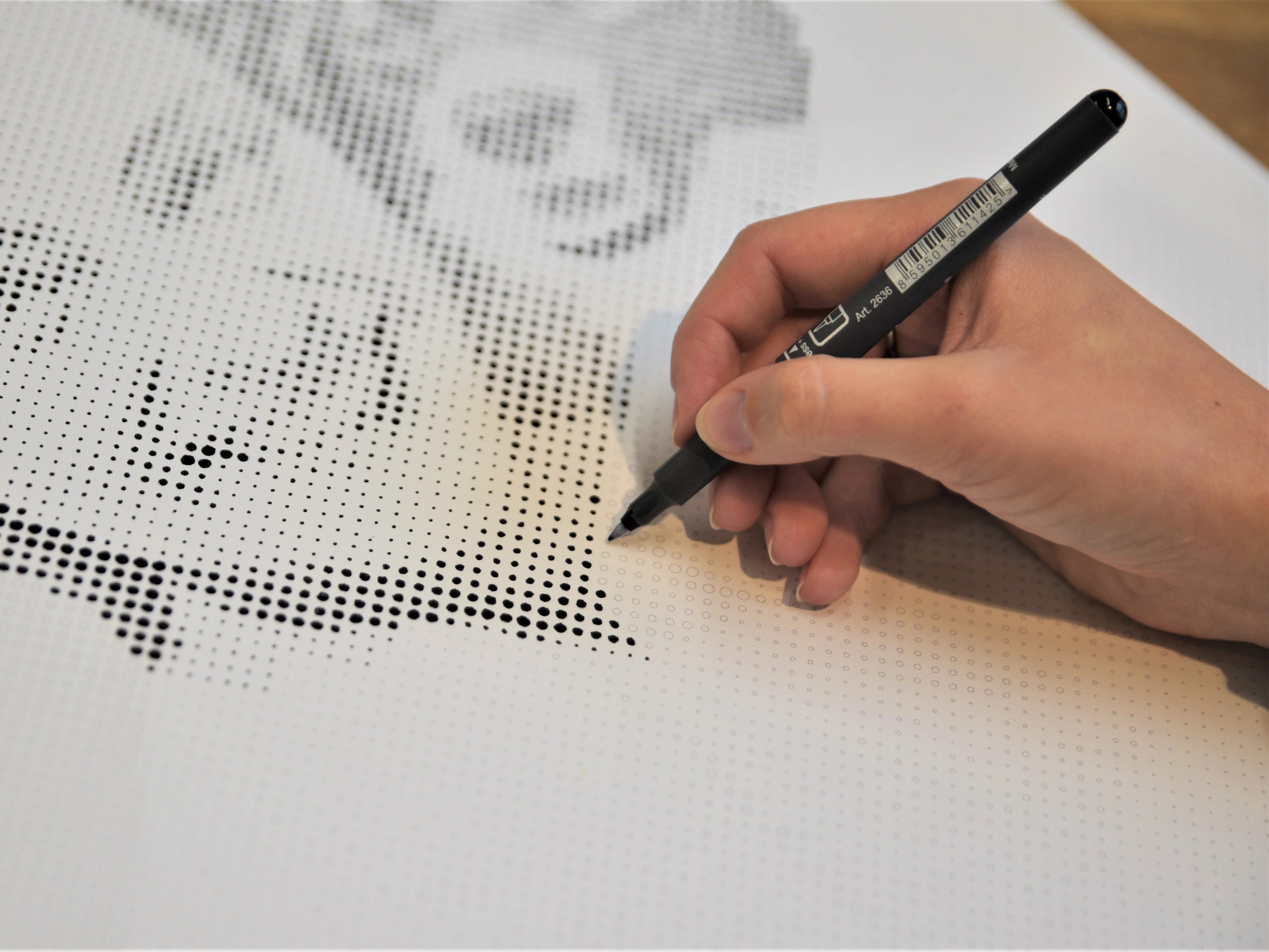 Hånd maler prikker med sort tusch på hvidt lærred med blomstermønster.